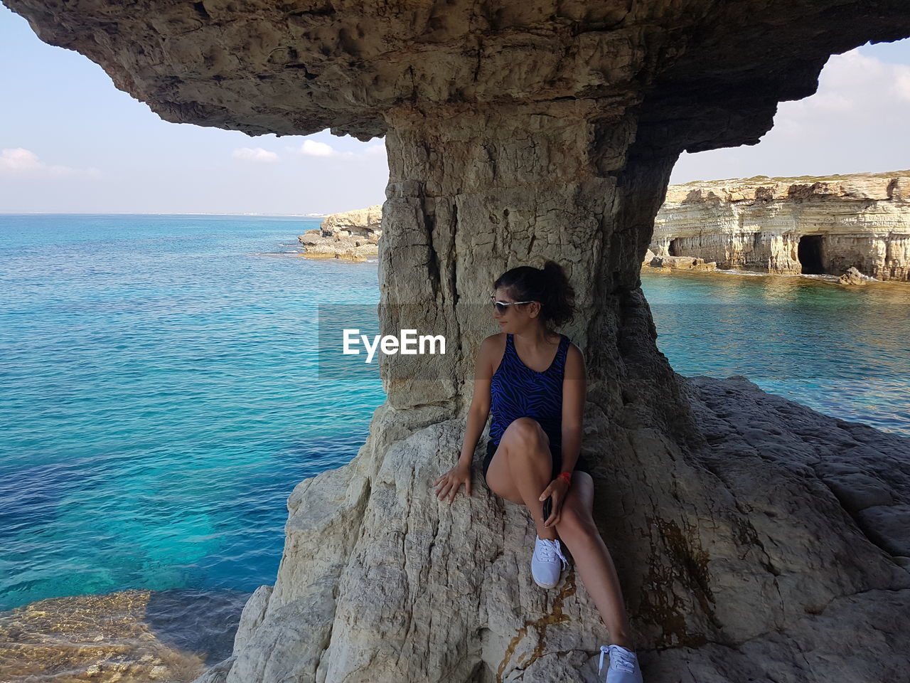 Woman sitting on rock by sea against sky