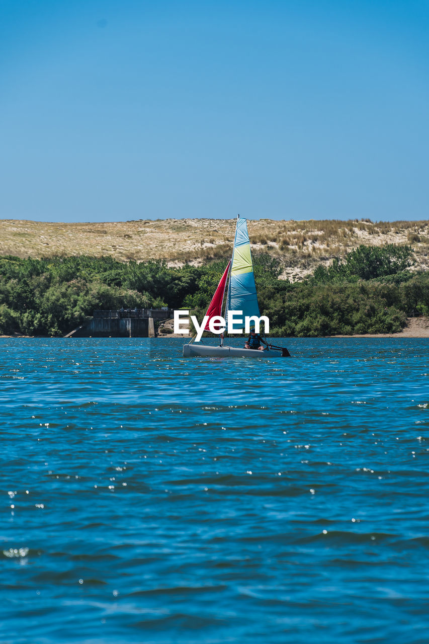 SAILBOAT SAILING IN SEA AGAINST CLEAR SKY