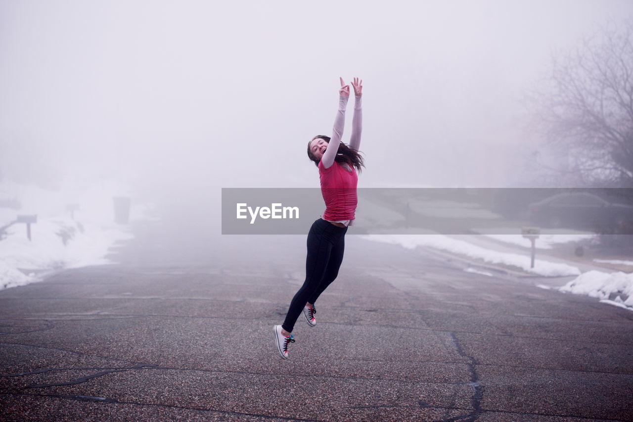 Young woman jumping on road during foggy weather