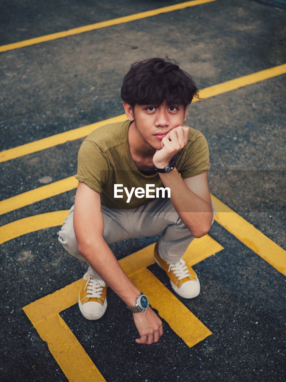 High angle view portrait of young man crouching on road