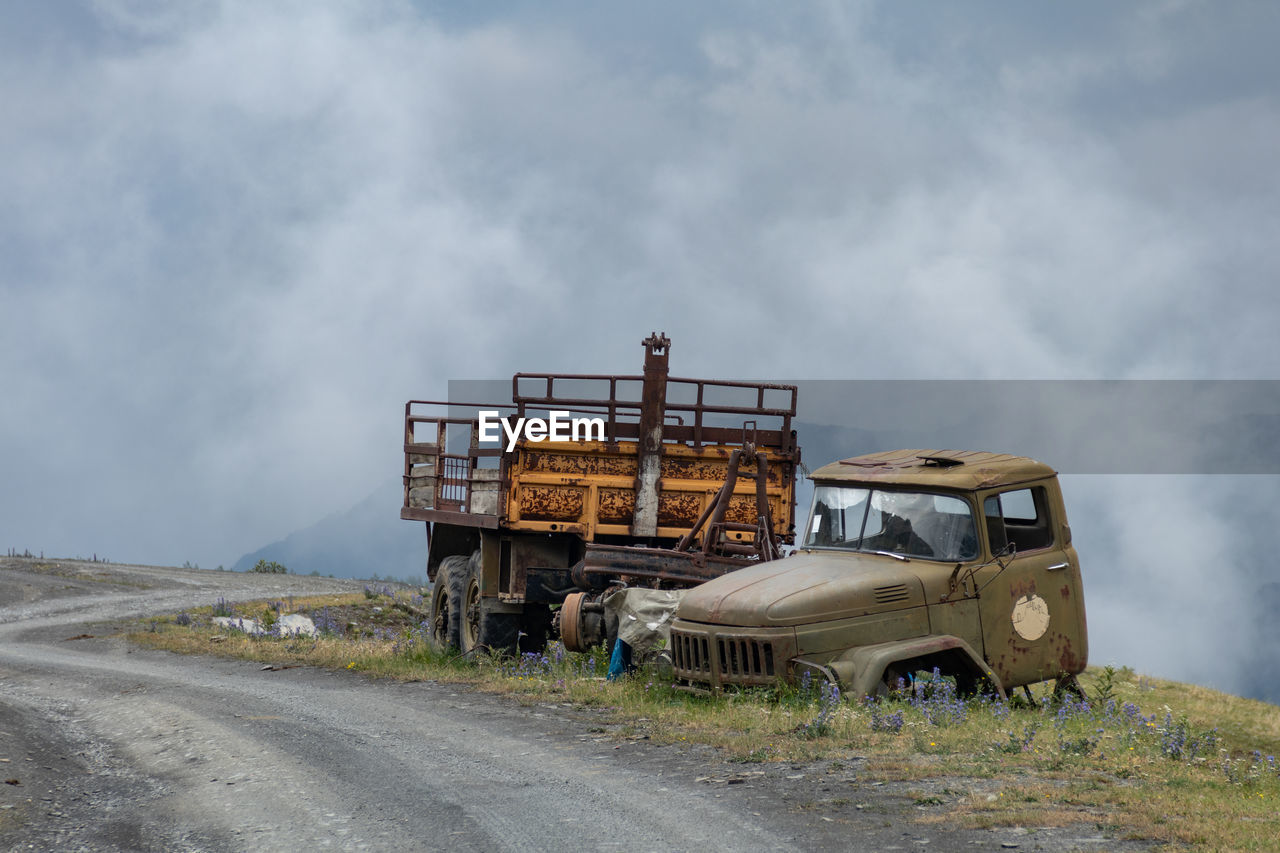 Abandoned truck on road against cloudy sky