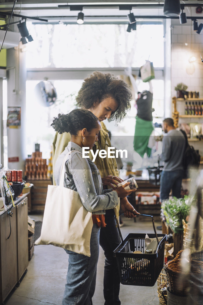 Man and woman discussing over jar while standing with shopping basket at store