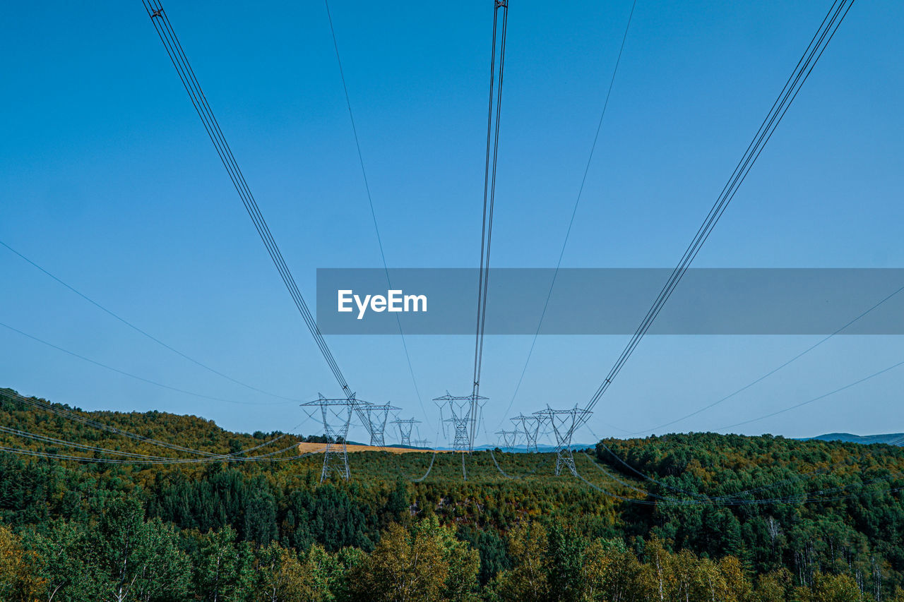 Electricity pylons on land against clear blue sky
