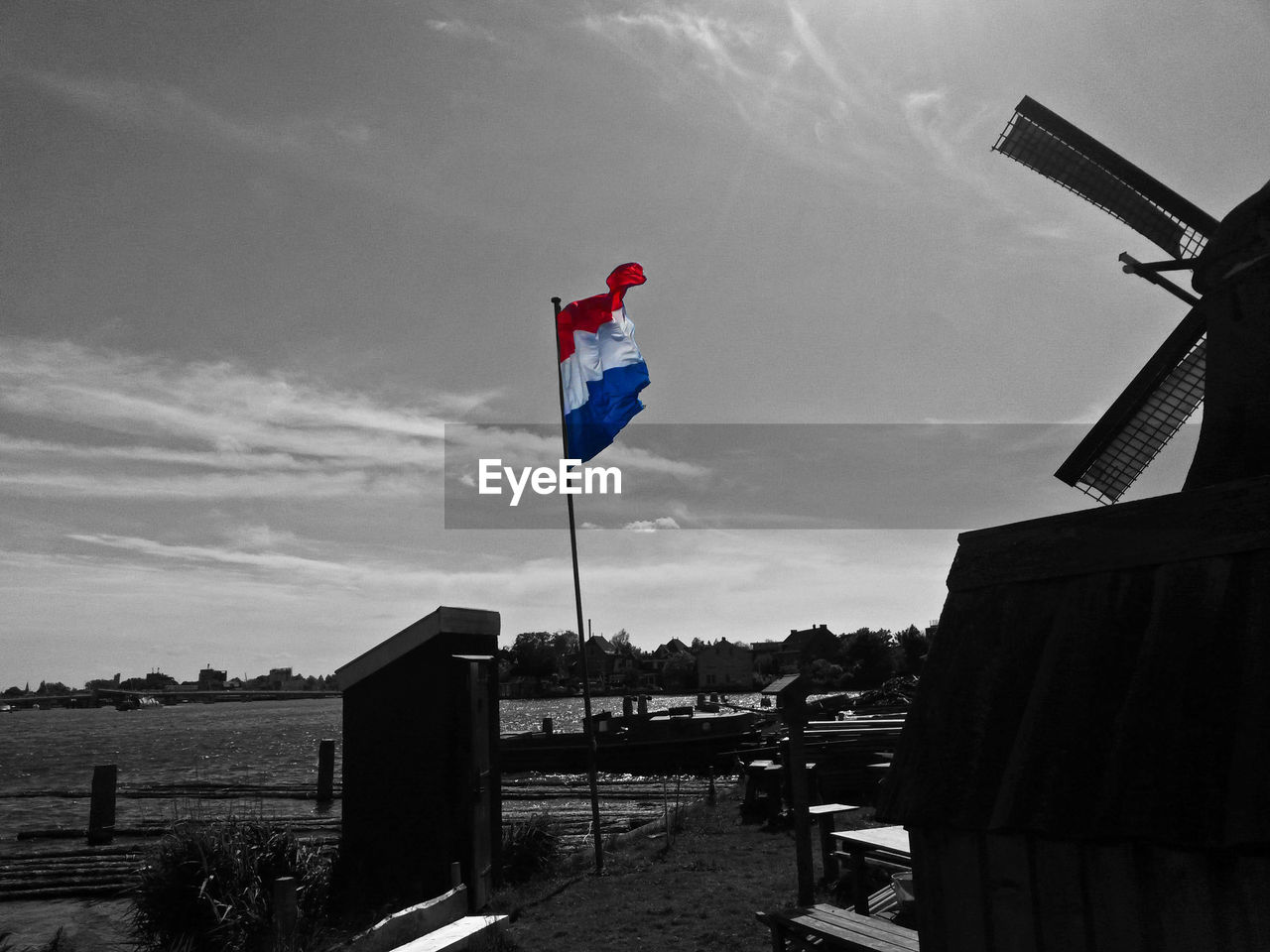 Dutch flag by traditional windmill at lakeshore against sky