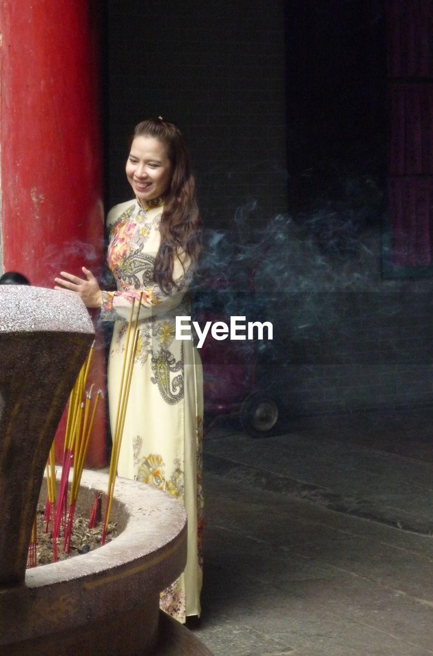 Happy woman standing by incenses at temple