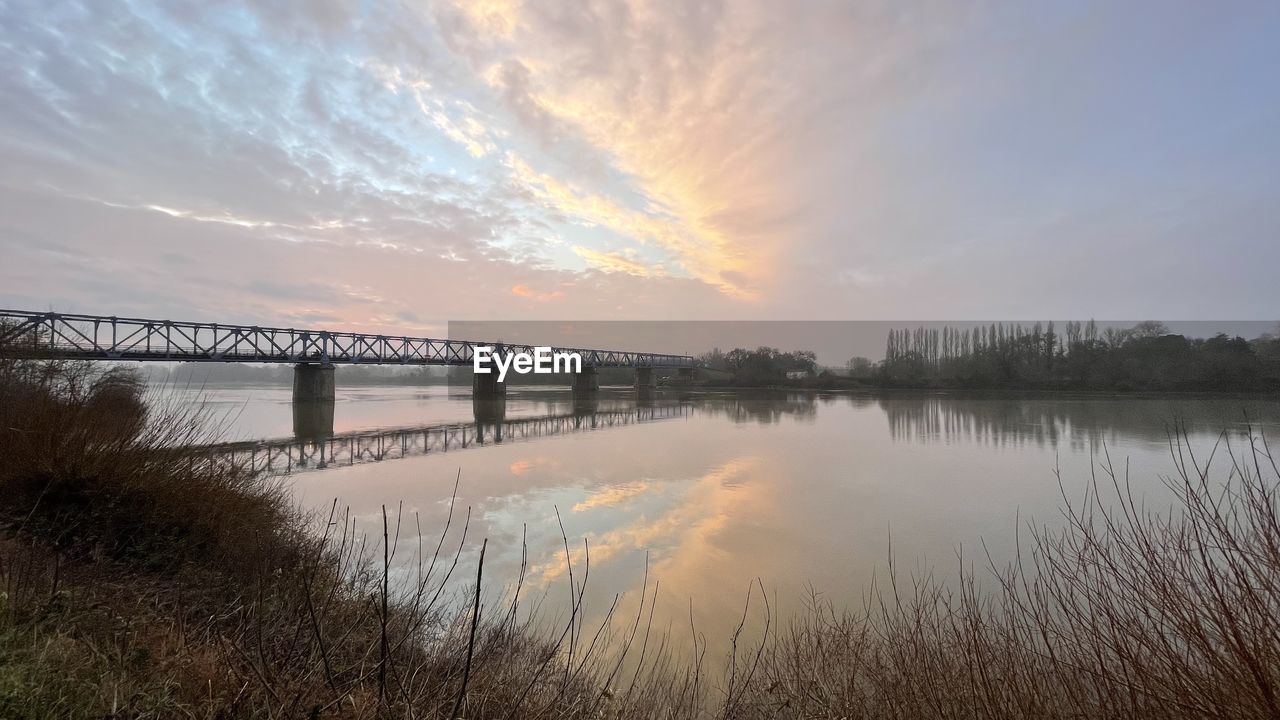 water, sky, morning, reflection, nature, cloud, dawn, sunrise, beauty in nature, scenics - nature, architecture, tranquility, environment, river, landscape, built structure, tranquil scene, no people, plant, bridge, sun, horizon, land, twilight, travel destinations, outdoors, idyllic, reservoir, beach, travel, sunlight, fog, non-urban scene, grass, tourism, tree, shore