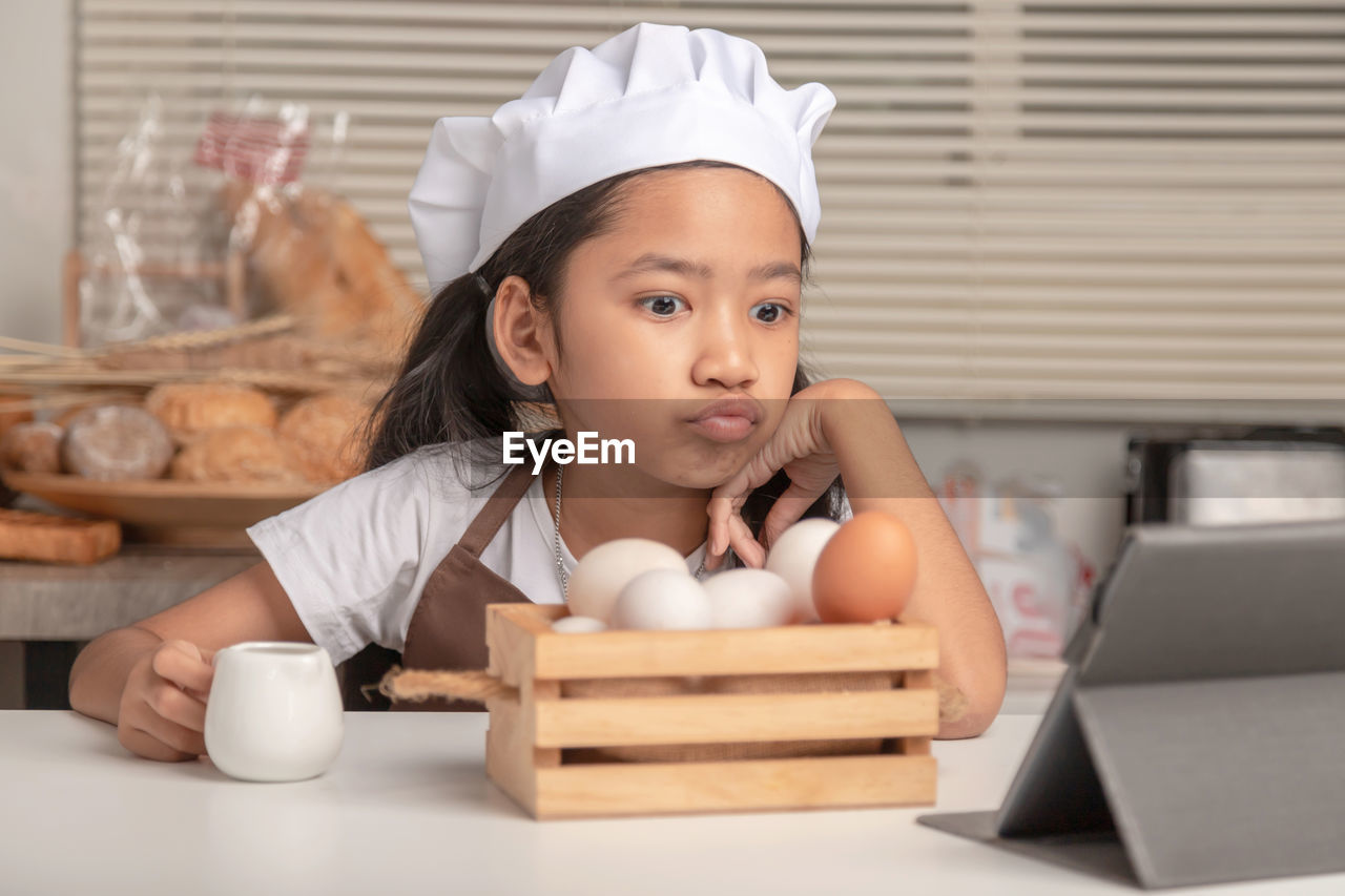 Cute girl looking at eggs on table at home