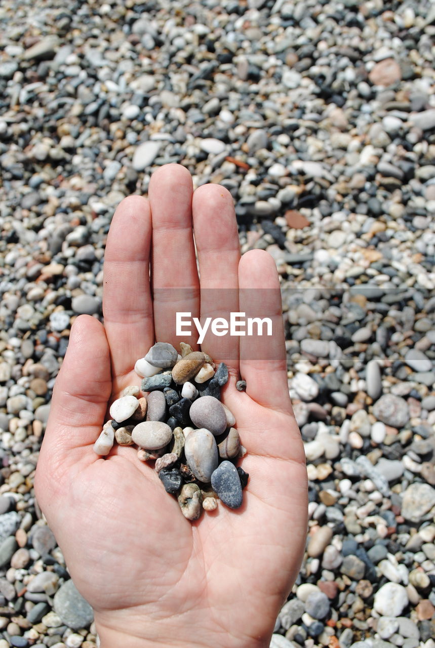 HIGH ANGLE VIEW OF HAND HOLDING PEBBLES