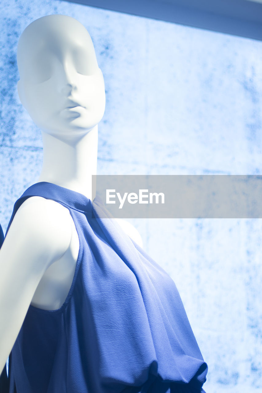 CLOSE-UP OF WHITE MANNEQUIN AGAINST BLUE STORE