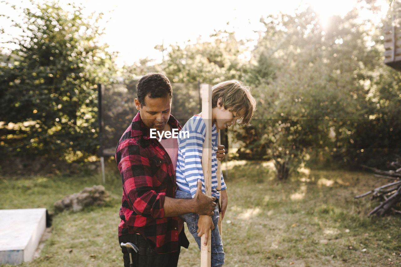 Side view of father helping son balance on wooden sticks in yard