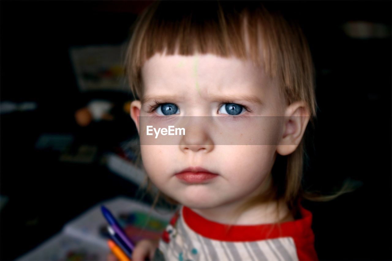 Close-up portrait of girl holding crayons at home