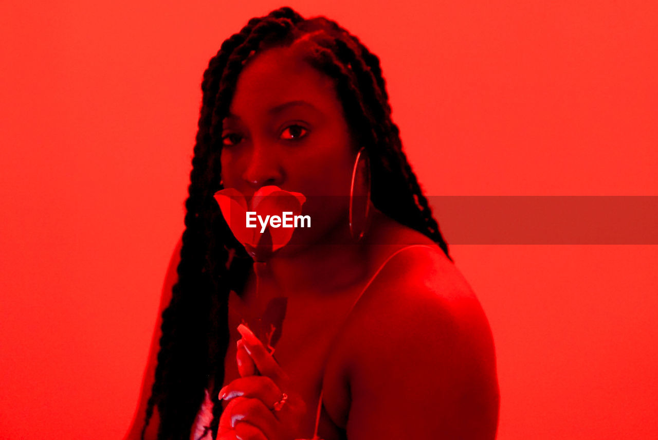 Portrait of beautiful braided black young woman against red background