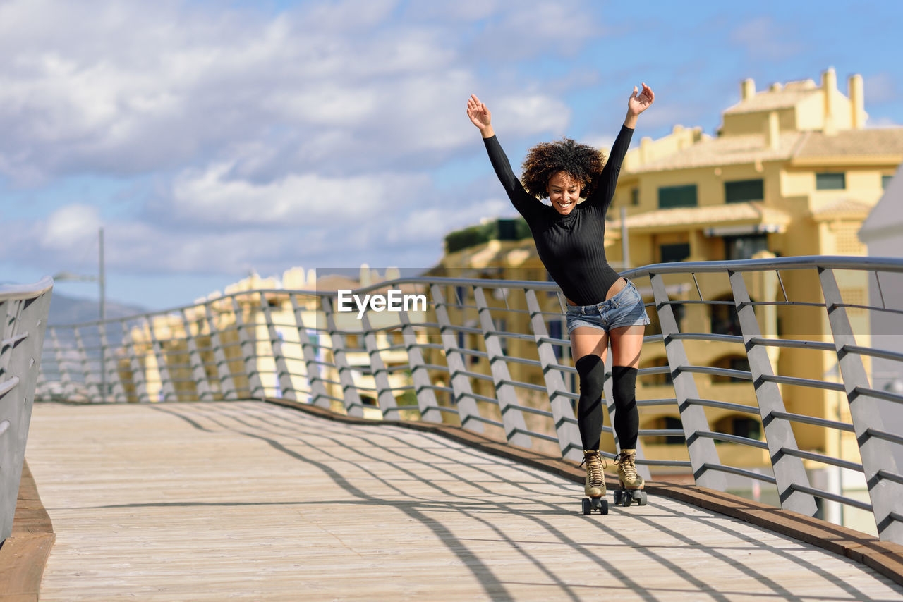 Happy woman with arms raised roller skating on bridge in city