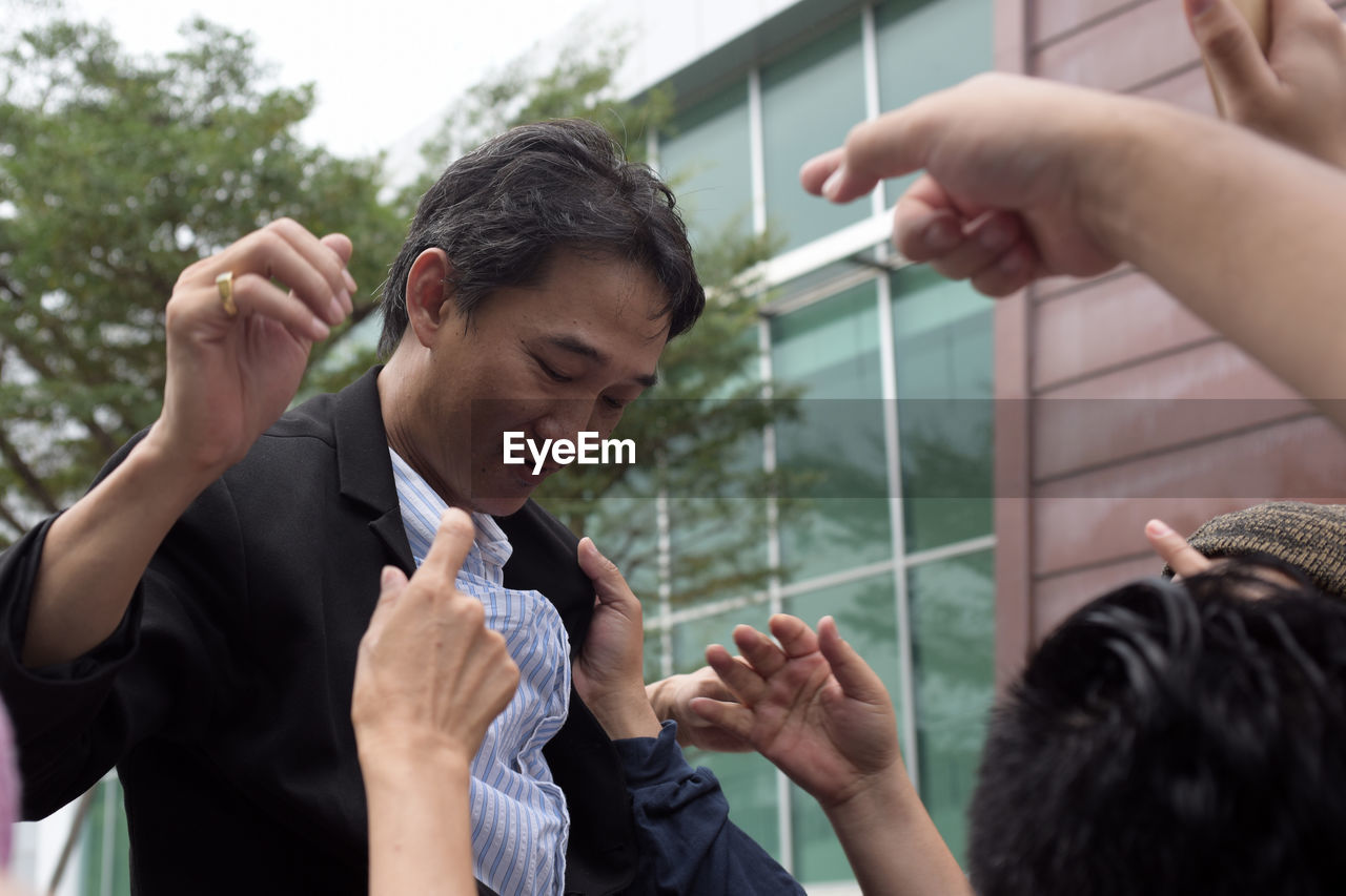 Low angle view of colleagues hitting businessman against sky
