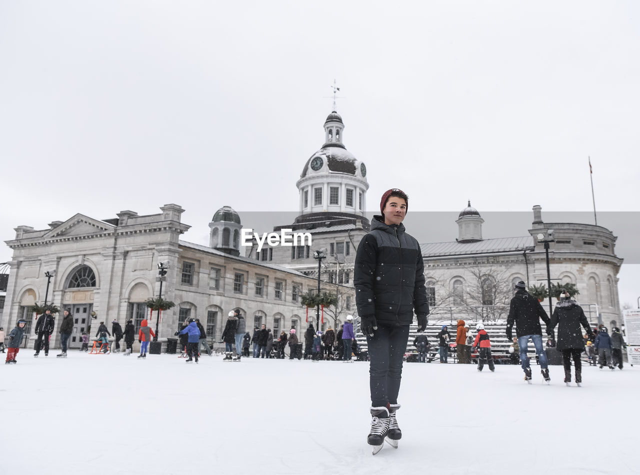 Teenage boy standing on outdoor skating rink on a cloudy day.