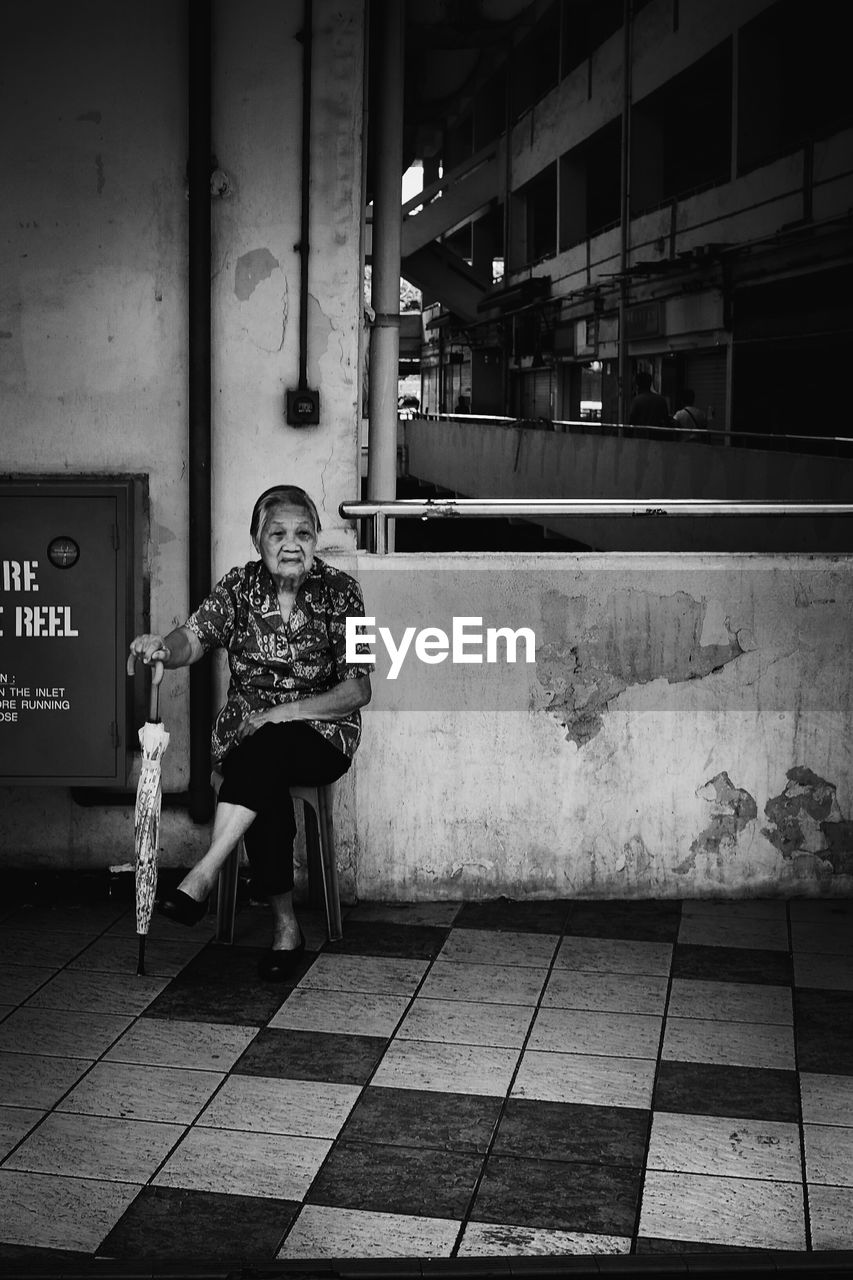 Senior woman with umbrella sitting in corridor