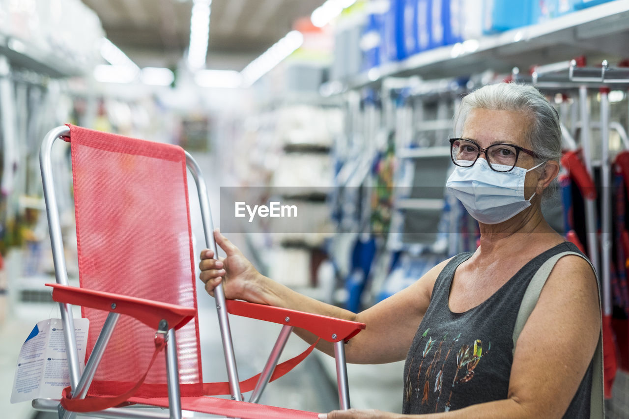 Portrait of senior woman with protective face mask holding chair in store