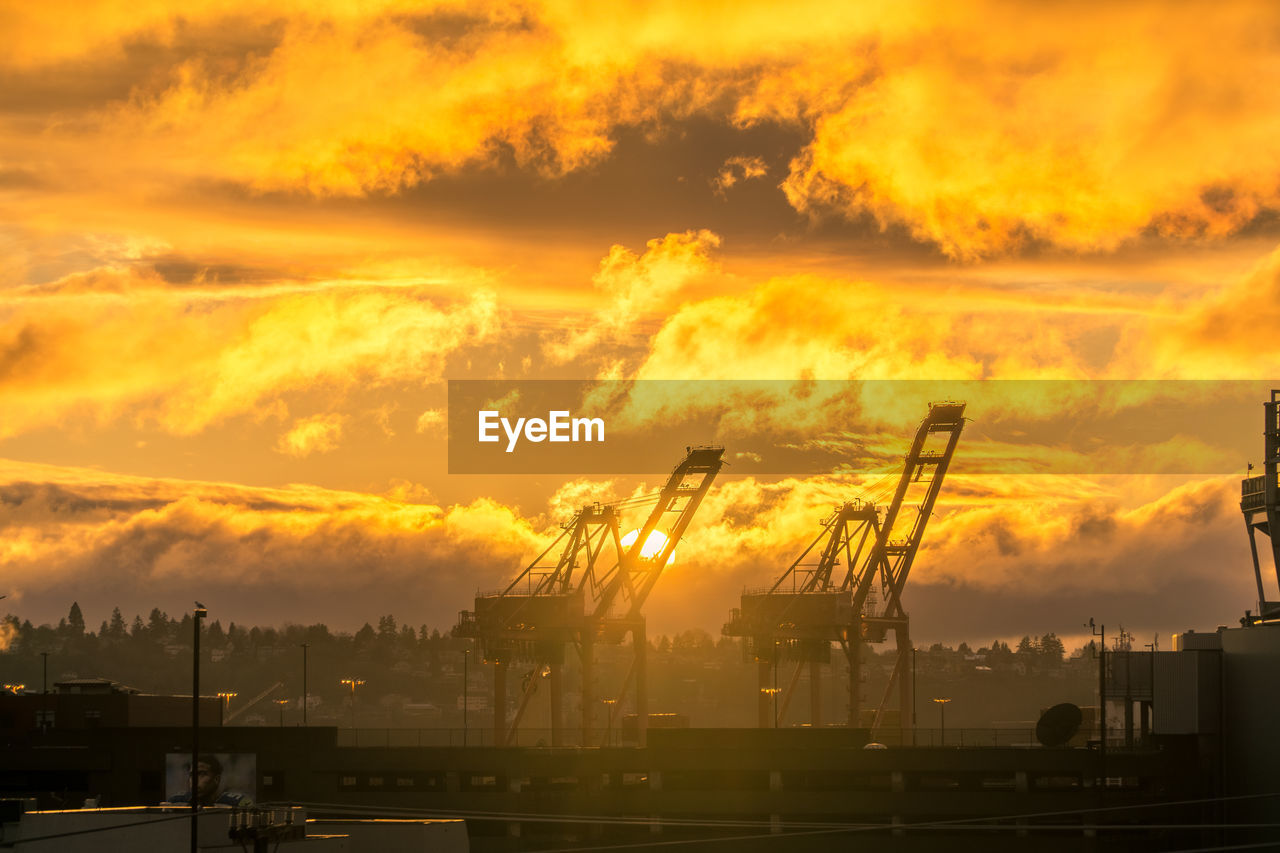 Silhouette cranes against orange sky