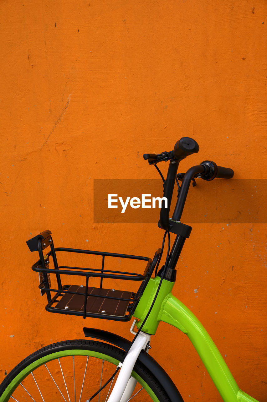 Close-up of bicycle parked against orange wall