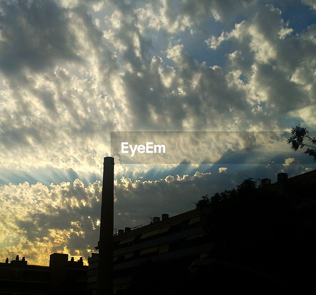 Low angle view of silhouette smoke stack against cloudy sky