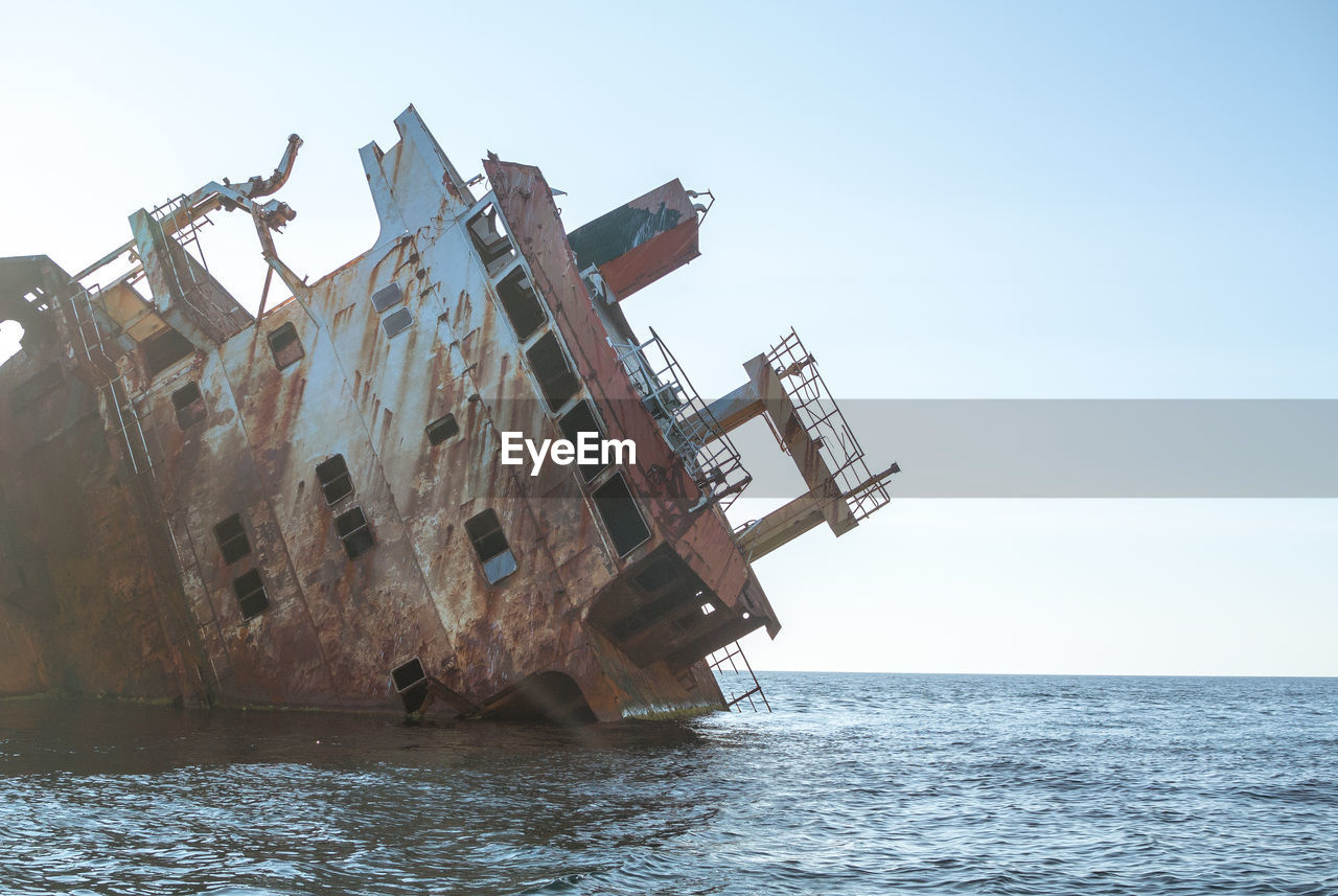 ABANDONED BOAT ON SEA AGAINST CLEAR SKY