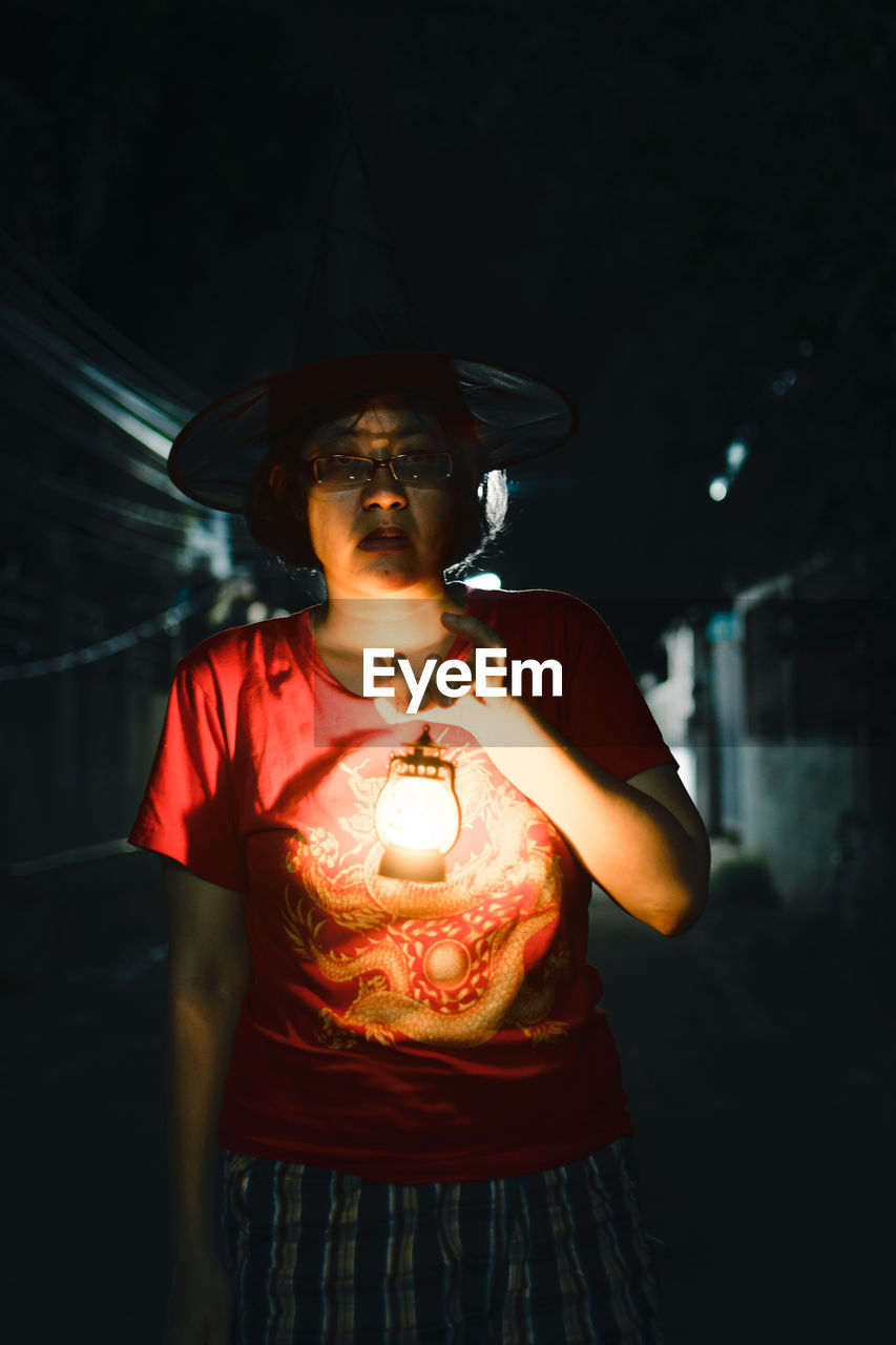 Woman wearing hat standing against illuminated lamp at night