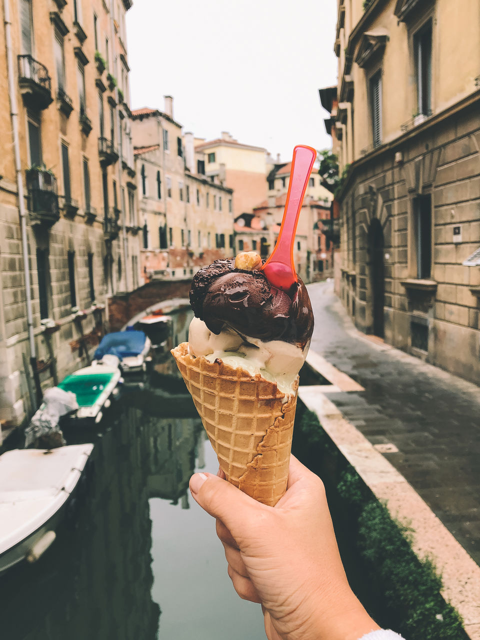 CROPPED IMAGE OF WOMAN HOLDING ICE CREAM CONE AGAINST CANAL