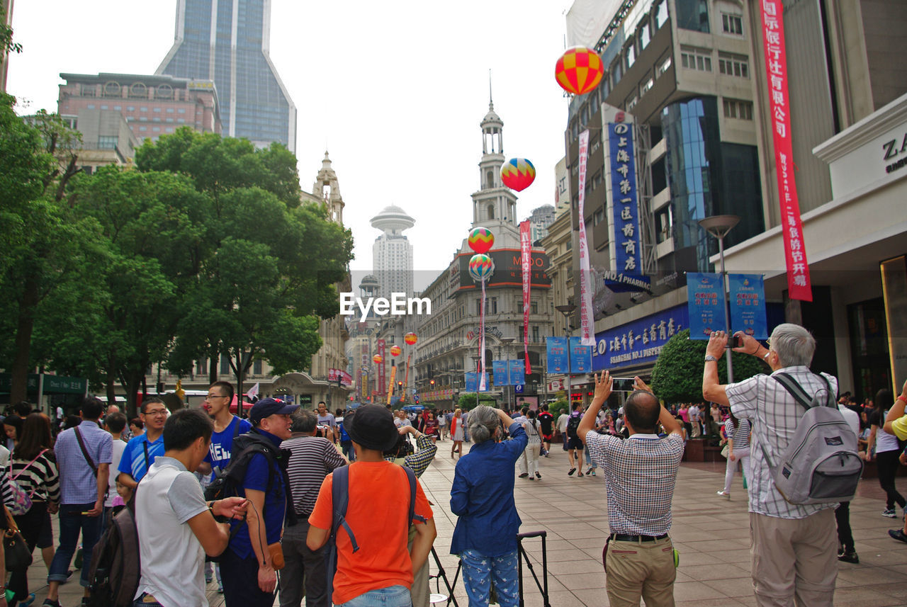 PEOPLE WALKING ON ROAD IN CITY AGAINST SKY