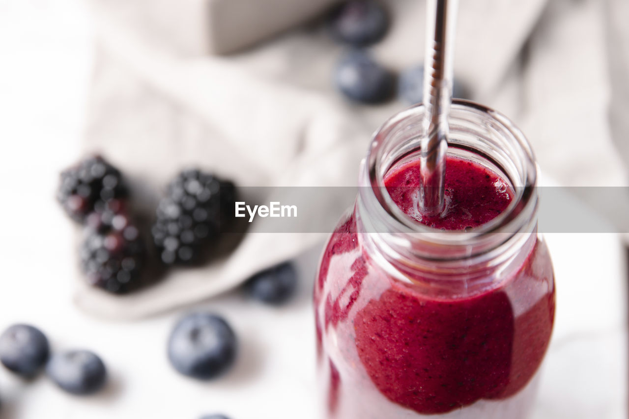 Fresh homemade smoothie made from berries, in a glass bottle with a metal straw.