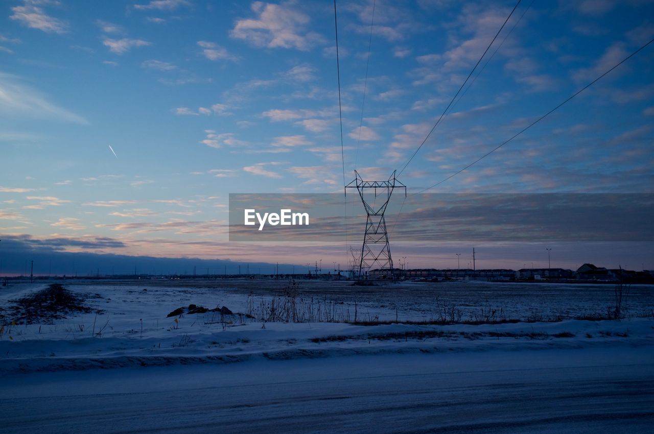 Silhouette electricity pylon on snowcapped field at sunset