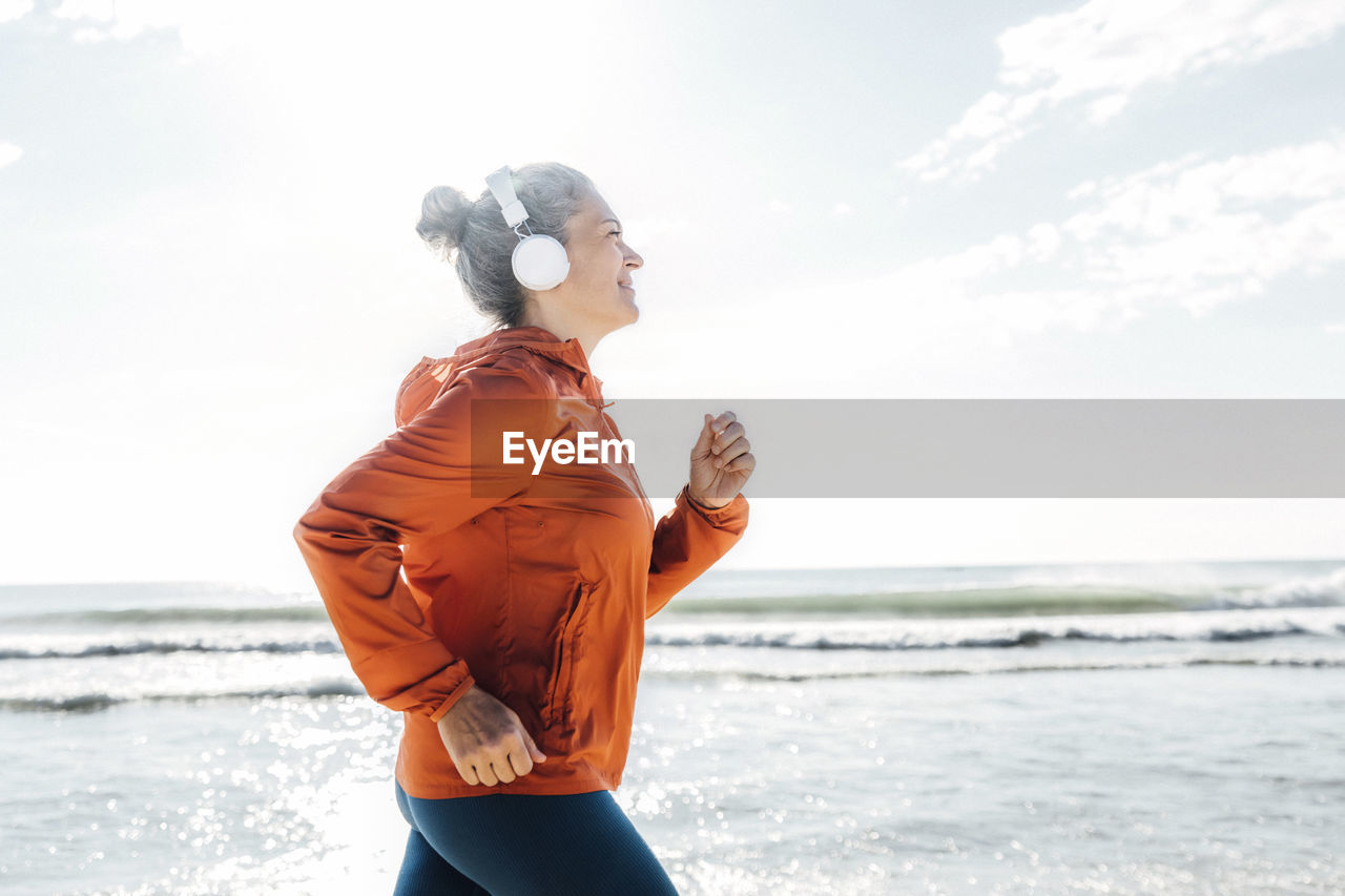 Woman wearing headphones jogging by sea on sunny day