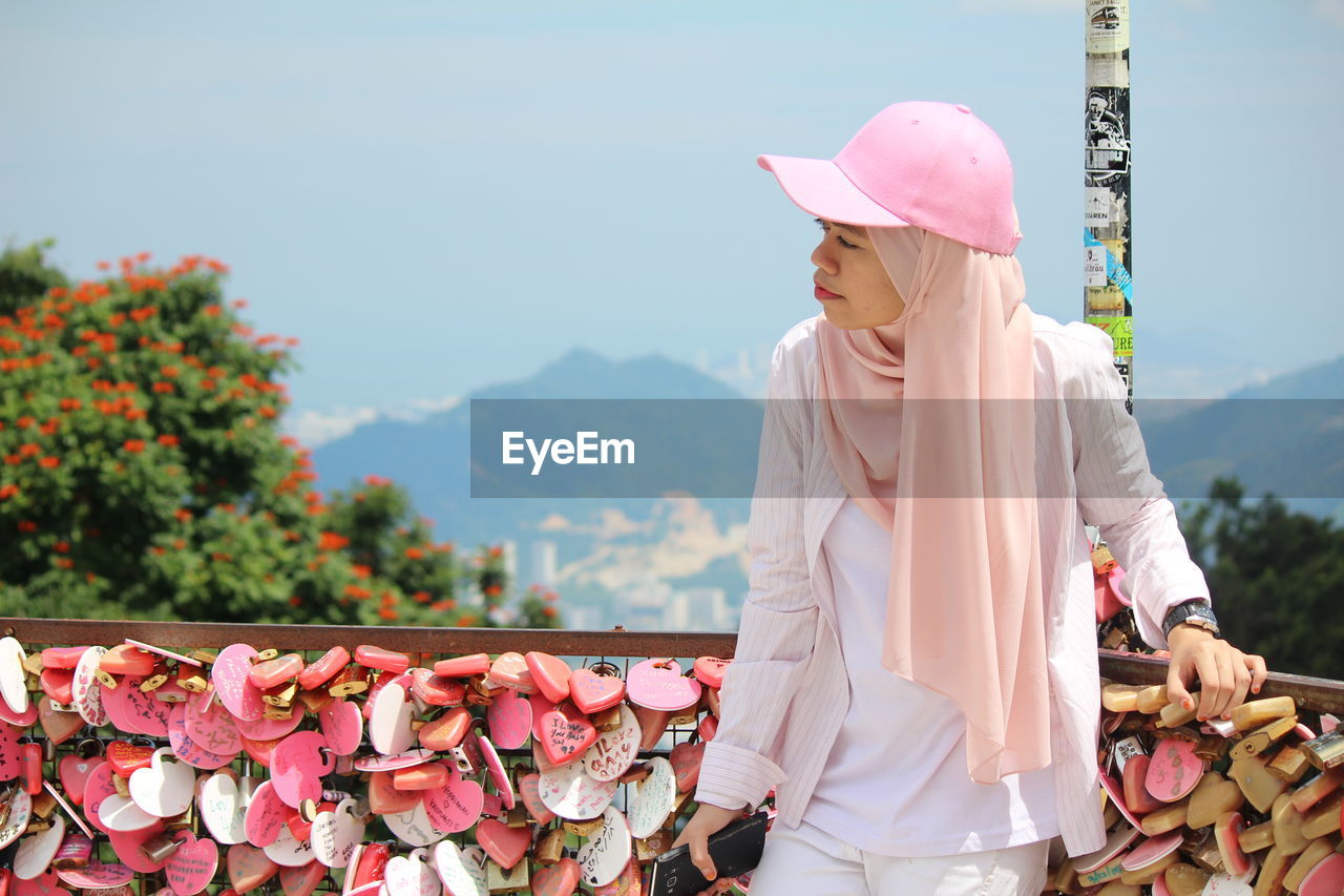 Young woman standing against railing with love locks