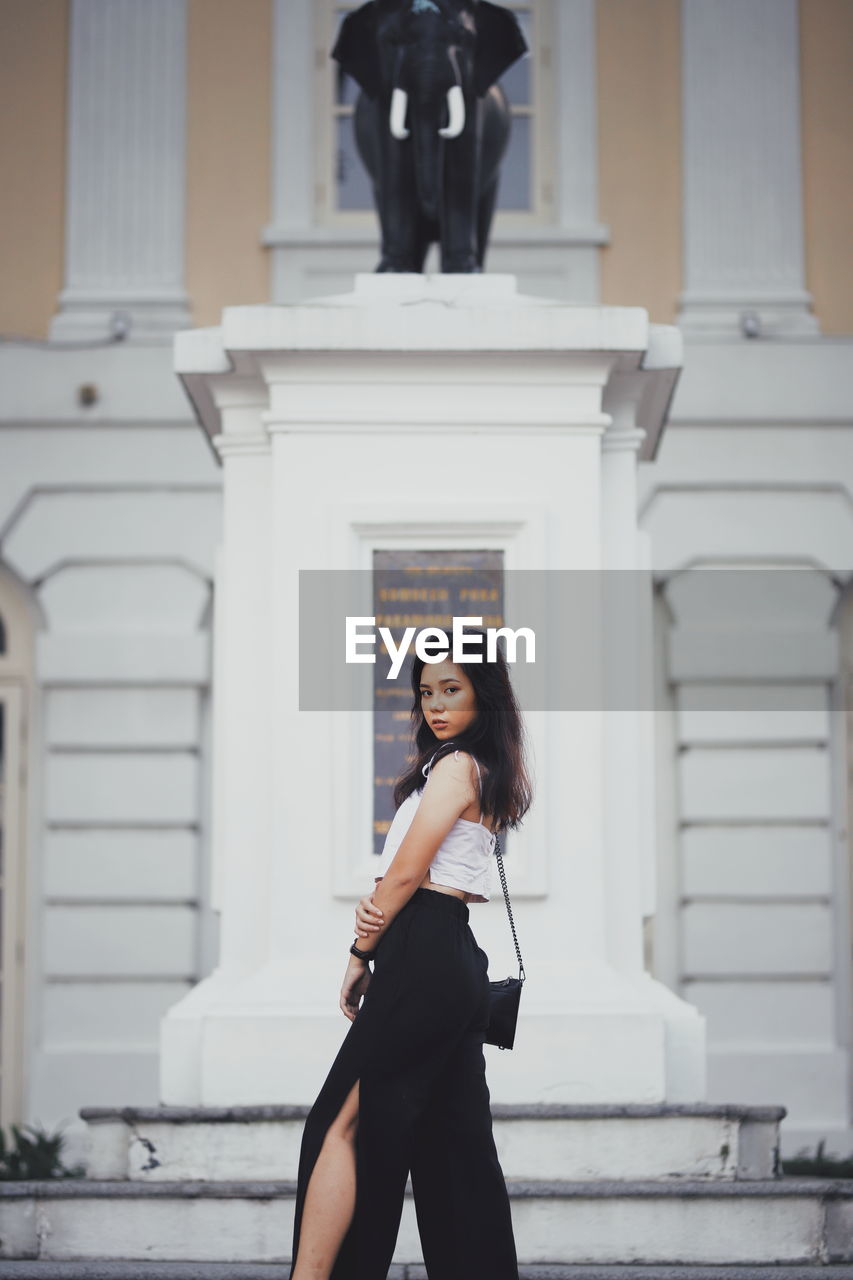 Portrait of young woman standing against building on city 