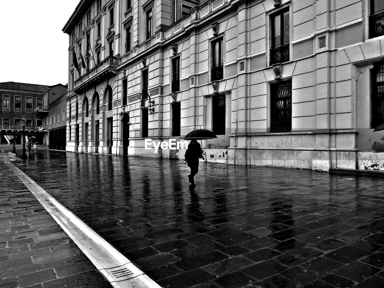 Person with umbrella walking on wet street by building