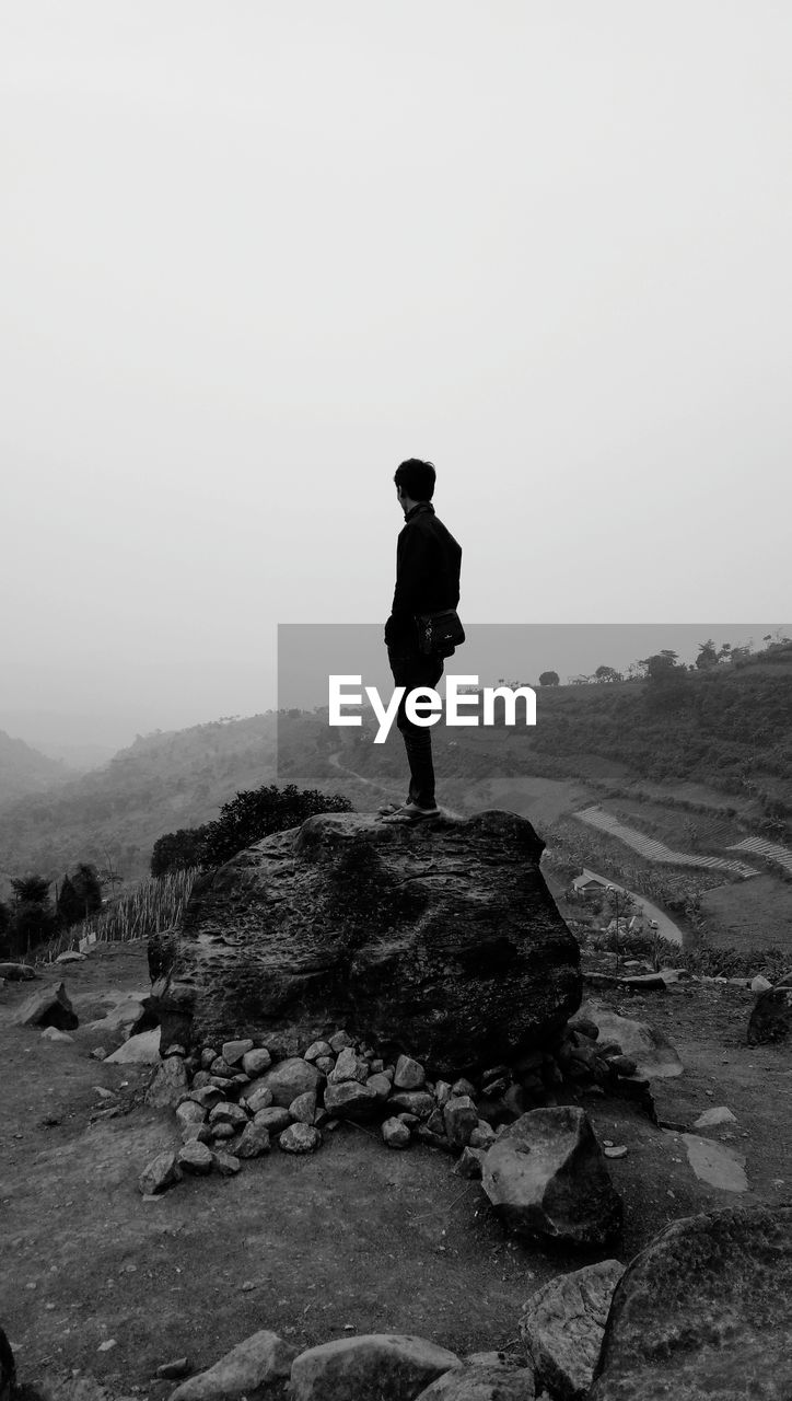 Man standing on rock against sky