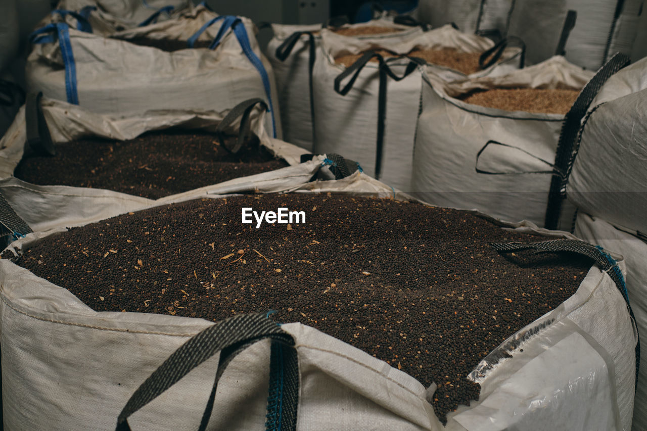 Huge bags with black grain crops stored in stock in industrial facility of factory