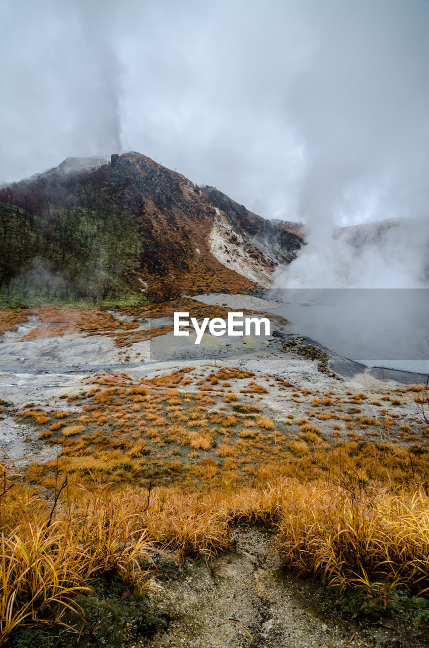 Scenic view of mountain by hot spring against sky