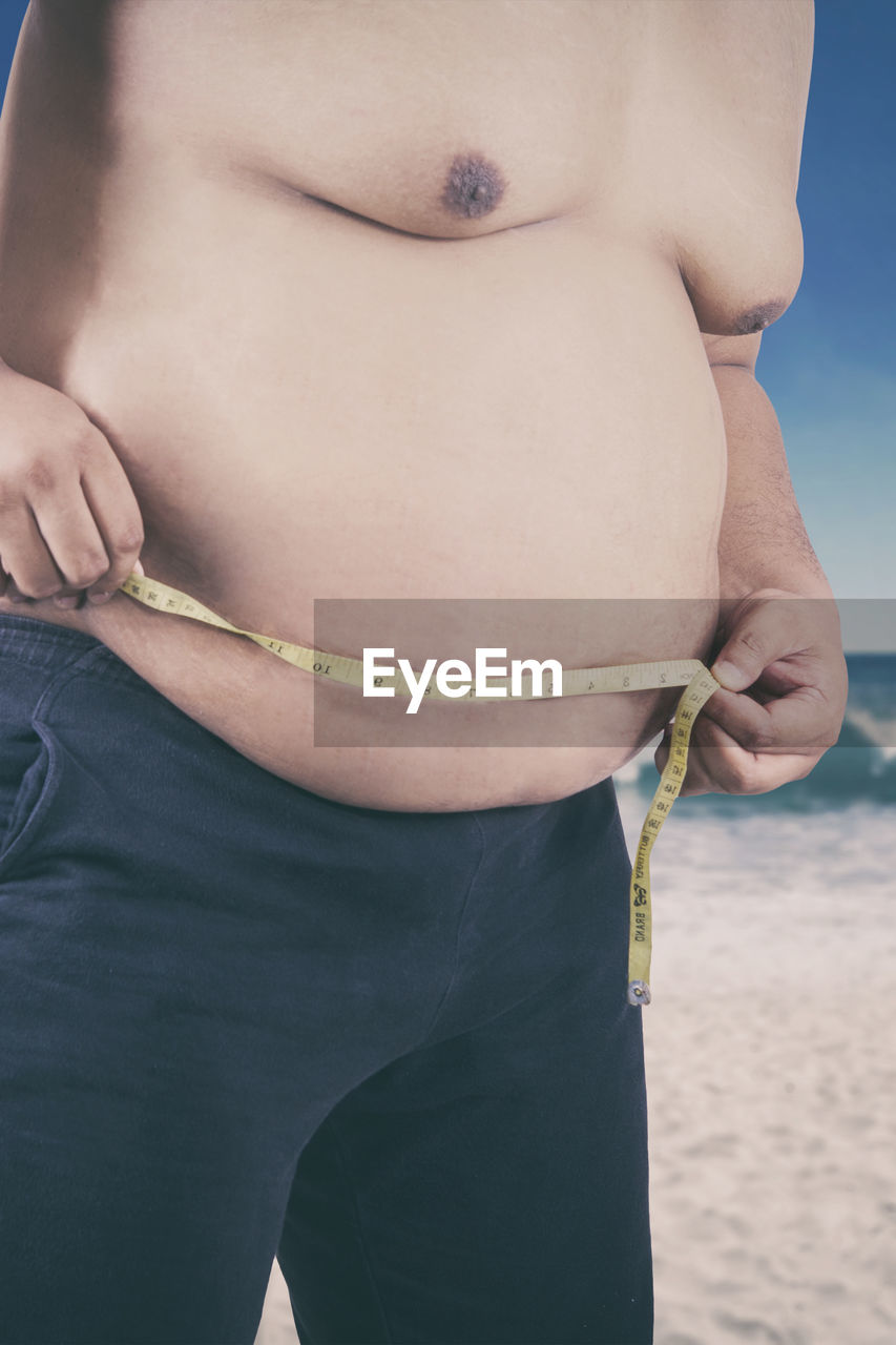 Man measuring abdomen at beach