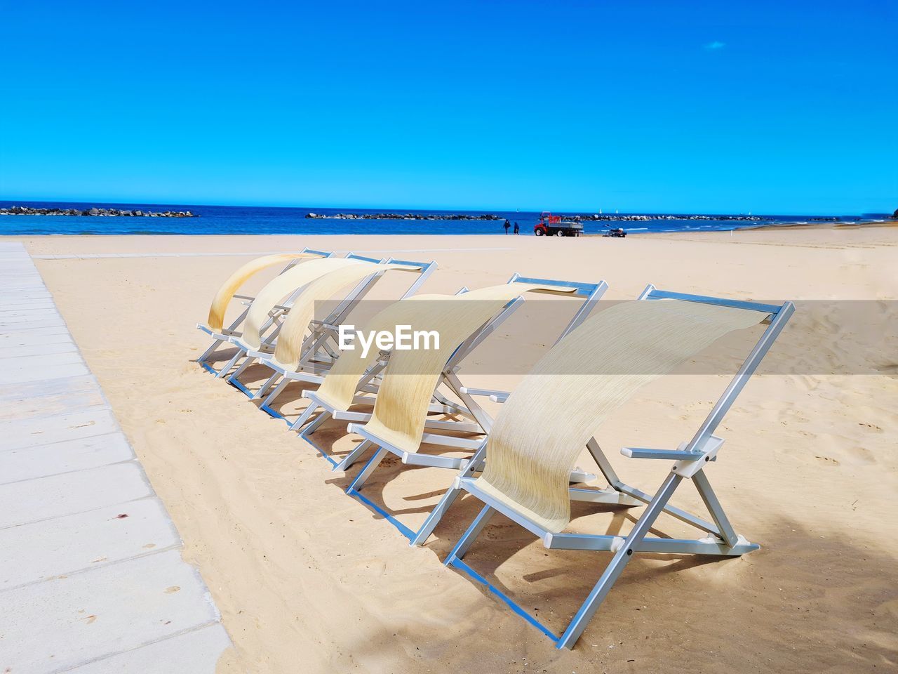 land, chair, beach, sand, sky, water, seat, sea, nature, blue, furniture, clear sky, absence, horizon, no people, scenics - nature, horizon over water, tranquility, sunny, day, shore, summer, vacation, trip, deck chair, tranquil scene, sunlight, wood, travel destinations, lounge chair, empty, copy space, ocean, holiday, beauty in nature, relaxation, outdoors, outdoor chair, travel, natural environment, body of water, in a row, coast