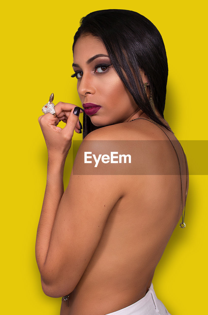 Side view portrait of topless young woman standing against yellow background