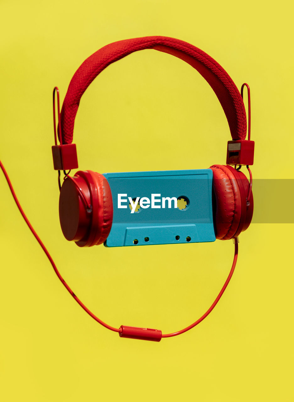 Old fashioned blue audio cassette in red headset showing concept of listening to music against yellow background in studio