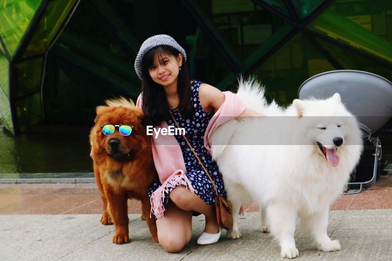 Portrait of smiling young woman with brown and white dogs on footpath