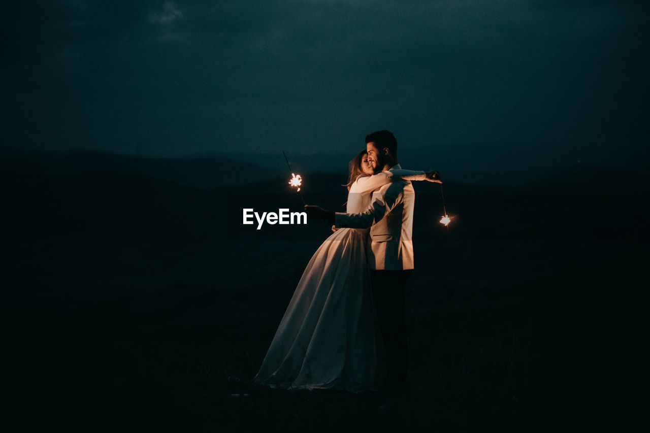 Young couple playing with fireworks at night after the wedding