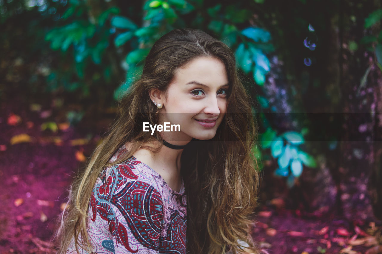 Portrait of smiling young woman standing against trees