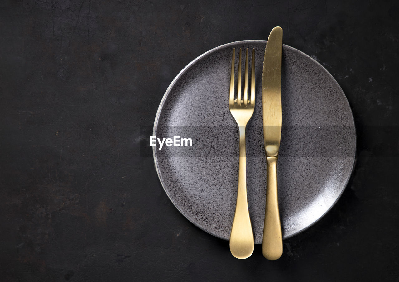 High angle view of knife and fork on plate against black background