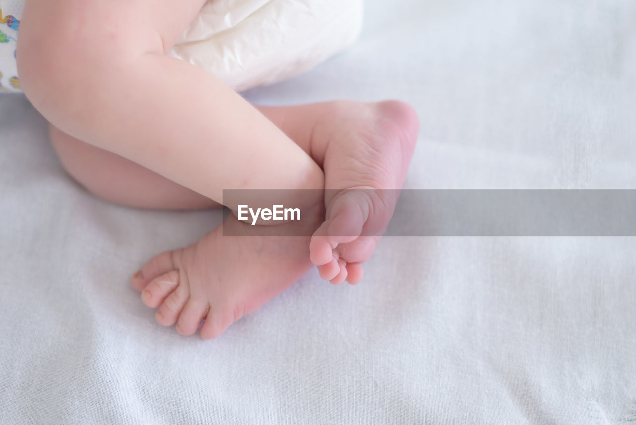 Low section of baby lying on bed at home