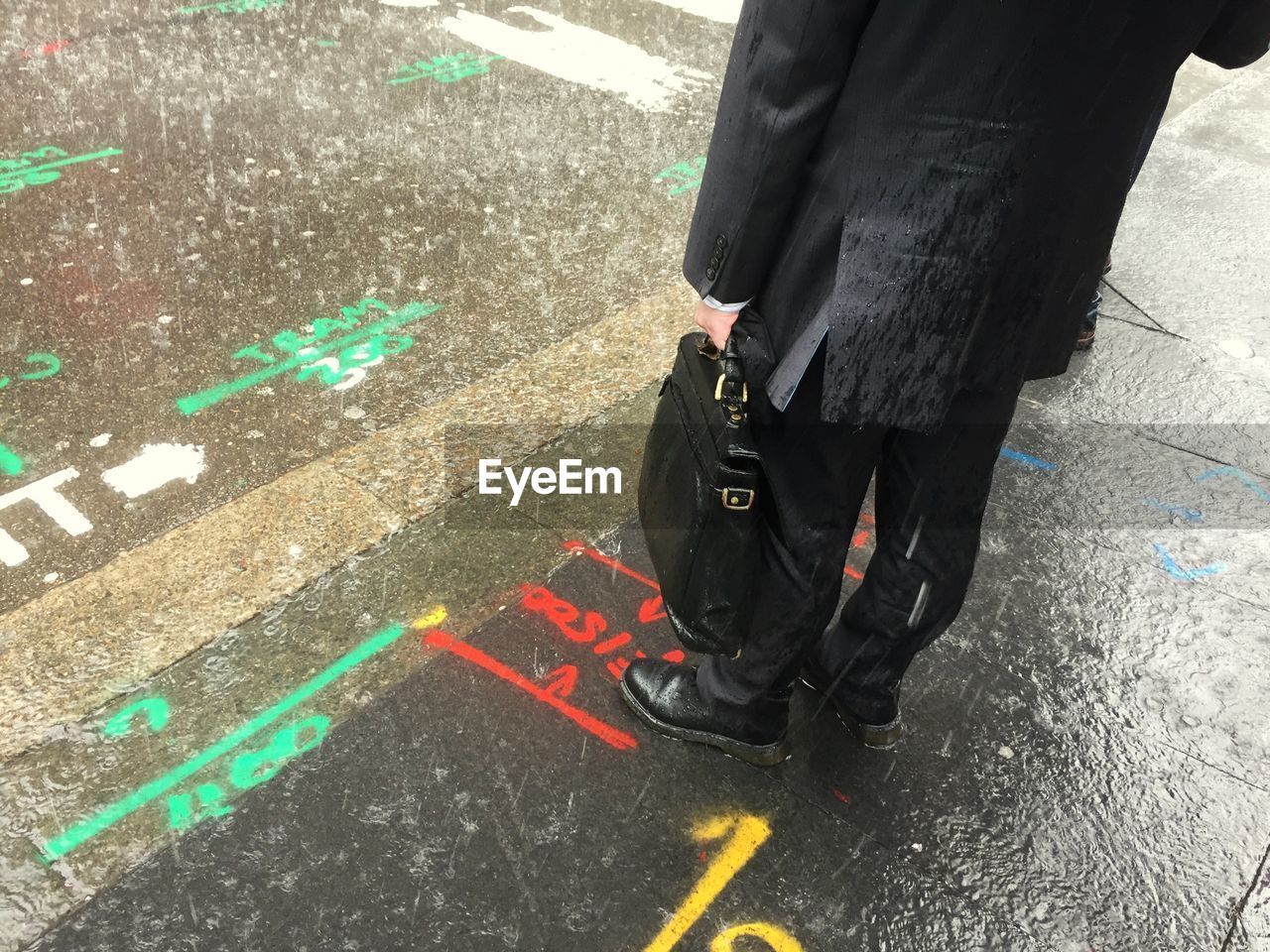 Low section of man standing on sidewalk with road markings in rain