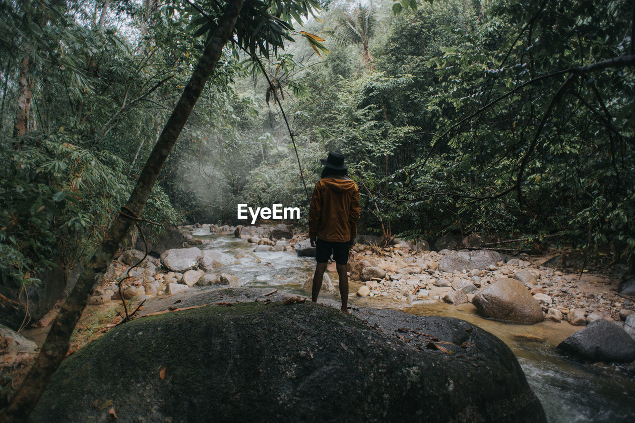 FULL LENGTH REAR VIEW OF MAN WALKING ON ROCK IN FOREST