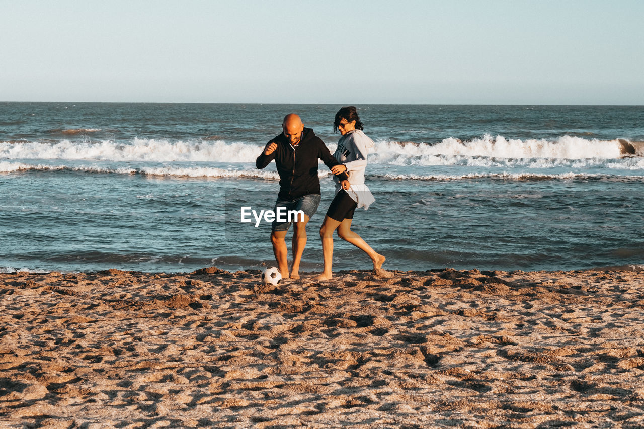 Couple playing at beach against sky