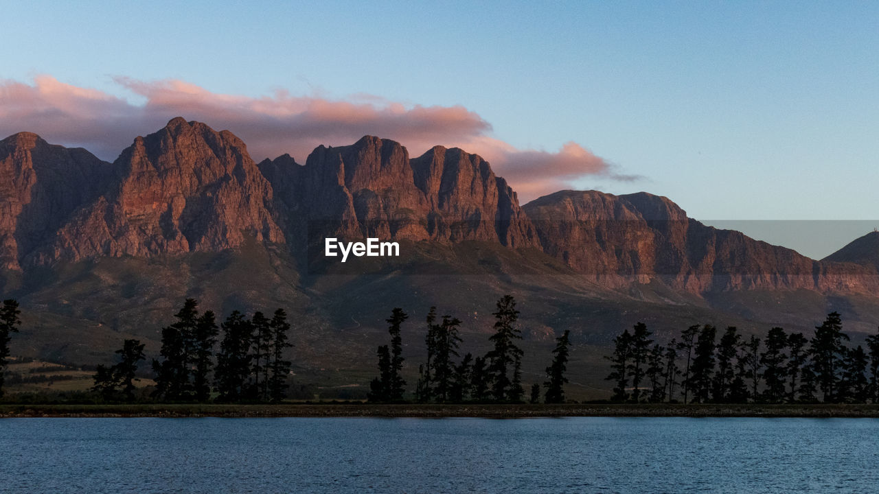 Scenic view of lake by mountains against sky during sunset